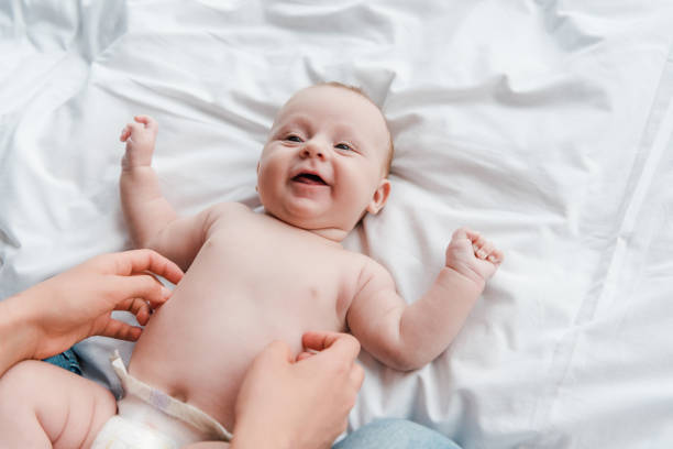 おむつで幸せな赤ちゃんの娘をくすぐる母親のトリミングされたビュー - tickling ストックフォトと画像