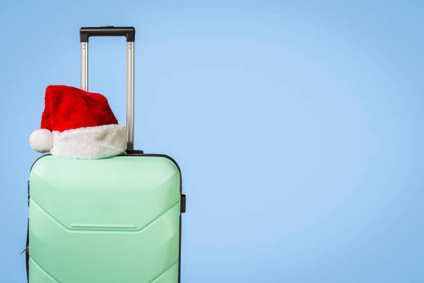 istock Plastic suitcase and Santa Claus hat on blue background. Concept 1183074455
