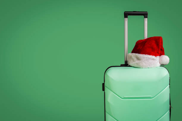 istock Plastic suitcase and Santa Claus hat on green background. Concep 1183075240