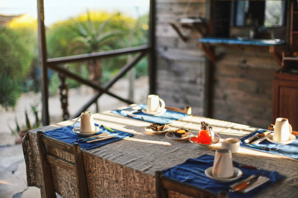 istock Morning sun shines on table with empty plates and coffee cups,  glass tea pot in middle, ready for morning breakfast, blurred green foliage in background - tropical holiday resort 1183079368
