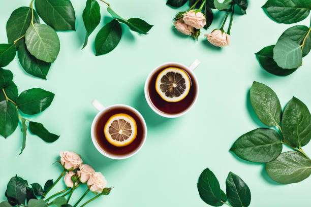 Mint background with two cups of tea and flowers. Food-drink mint concept. Two cups of hot tea with lemon surrounded by leaves and pink roses. Flat lay, top view, copy space. tea crop photos stock pictures, royalty-free photos & images