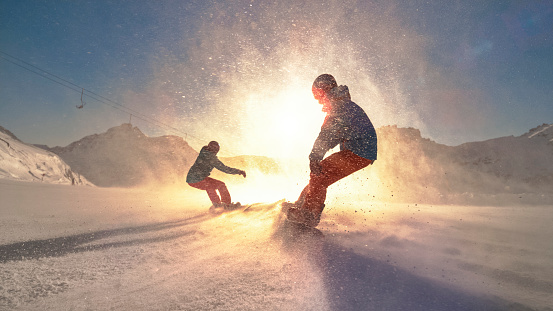 Man and woman snowboarding on mountain slope during sunset.
