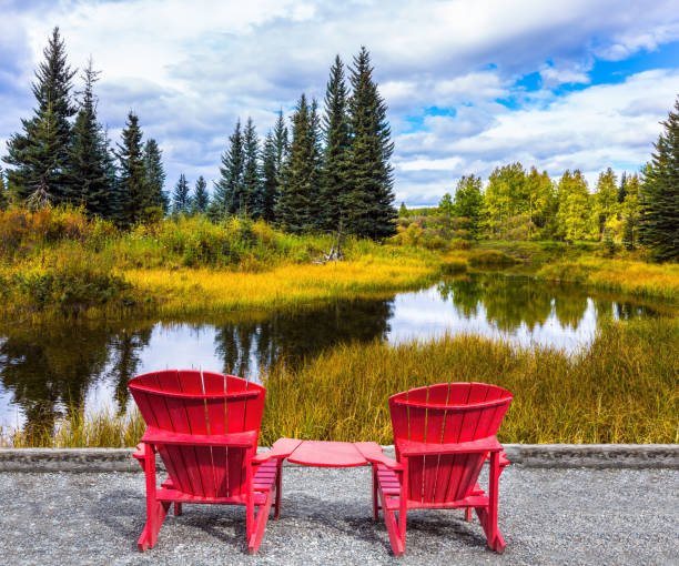 Quiet lake surrounded by dry yellow grass. Two red sun loungers for tourists on the lake. The Bighorn Highway in the Canadian Rockies. The concept of ecological, active and photo tourism