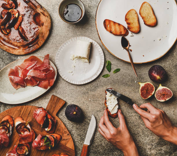 istock Crostini with prosciutto, figs and female hands spreading goat cheese 1183093130