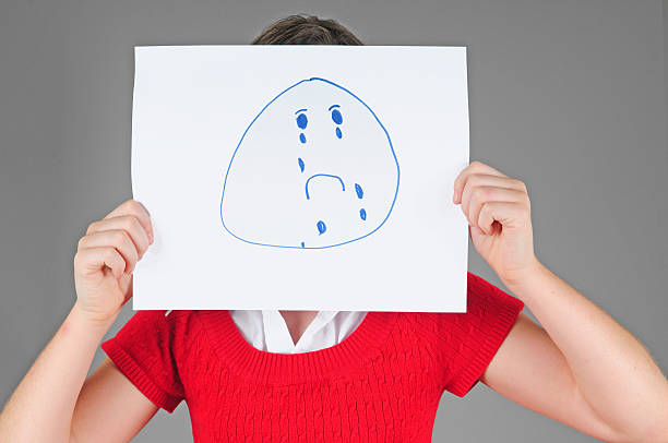 Sadness and disapproval concept - one man holding an anthropomorphic sad face covering his own face.