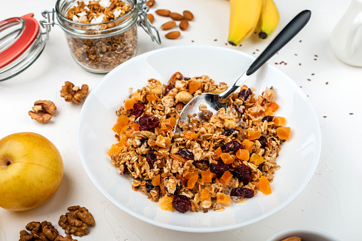 Granola muesli breakfast with with milk, dried apricots, cranberries, almonds and flax seeds in bowl on a white background. Healthy cereal breakfast