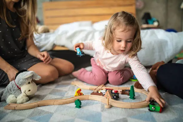 Photo of Toddler girl playing with wooden train on floor