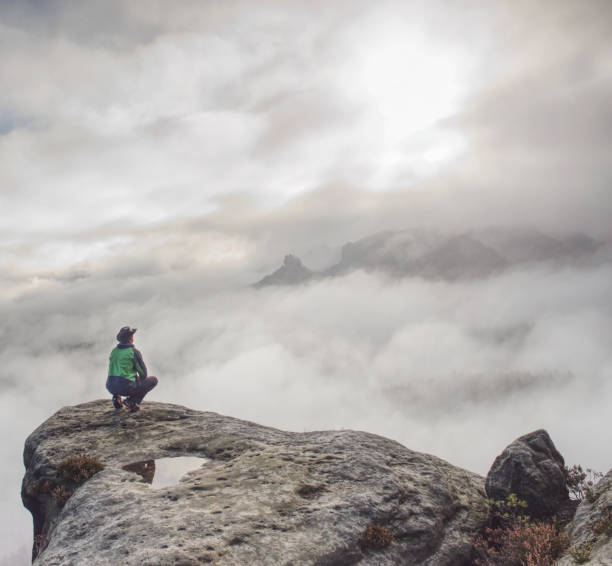istock Man sitting on cliff enjoying mountains and clouds landscape 1183101313