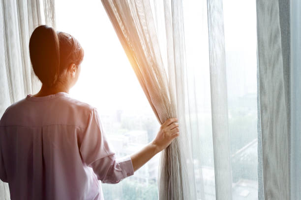 istock Woman opening curtains and looking out 1183103844