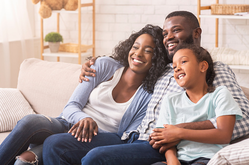 African american father, mother and daughter watching tv together, relaxing at home.