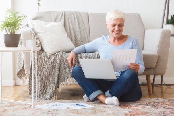 istock Old lady reading papers, sitting on floor with laptop 1183105309