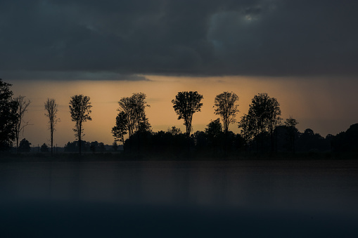 Tree silhouettes in the distance on a rainy summer evening at sunset in the Lithuanian countryside. Reflection on the gray roof of the car. With copy space for text