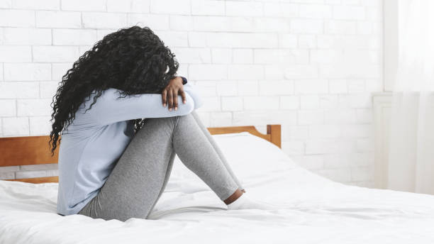 istock Depressed young girl sitting on bed, hugging her knees 1183110071
