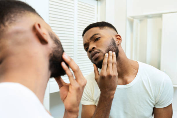 Concentrated african guy looking at his beard at bathroom mirror Need to shave. Concentrated african guy looking at his beard at bathroom mirror stubble male african ethnicity facial hair stock pictures, royalty-free photos & images