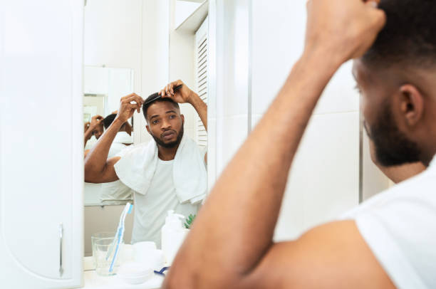 istock Young black man examining his hair, looking at bathroom mirror 1183114069