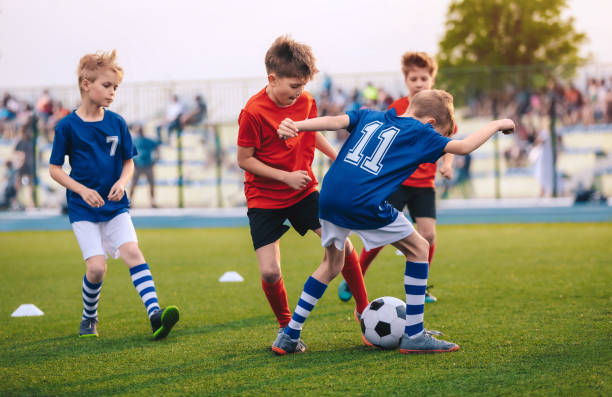 子供たちはフットボールボールを蹴る。男の子は草原でサッカーをする。背景の観客の両親。ユースプレイヤーは草のスタジアムでサッカーの試合を蹴る。ユースサッカートーナメント - youth league 写真 ストックフォトと画像