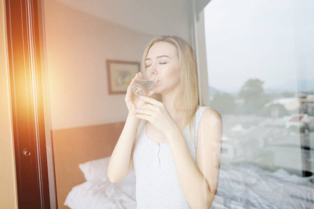 istock young woman drinks water after wake up with sun light on the balcony 1183117193