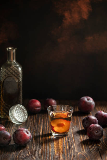 rakia lub rakija tradycyjna bałkańska brandy owocowa. śliwkowa brandy sljivovica w szklance i dekanter na drewnianym stole i ciemnym tle. pionowy. obszar kopiowania - vodka hard liquor bottle palinka zdjęcia i obrazy z banku zdjęć