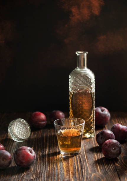 rakia o rakija tradizionale brandy di frutta balcanica. sljivovica di brandy di prugne in vetro e decanter su un tavolo di legno e sfondo scuro. verticale. spazio di copia - vodka hard liquor bottle palinka foto e immagini stock