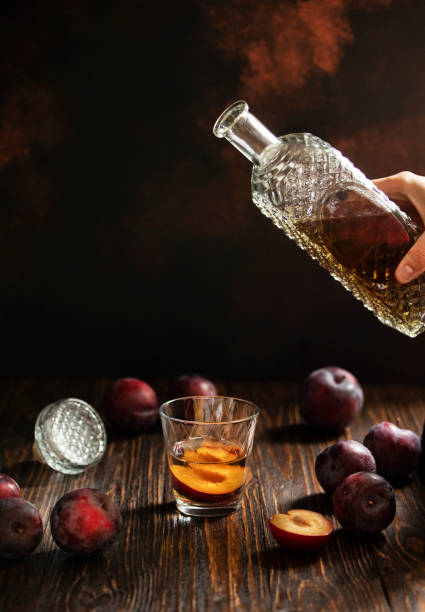 rakia o rakija tradizionale brandy di frutta balcanica. sljivovica di brandy di prugne in vetro e decanter su un tavolo di legno e sfondo scuro. rakia viene versata da una bottiglia in un bicchiere. verticale. spazio di copia - vodka hard liquor bottle palinka foto e immagini stock