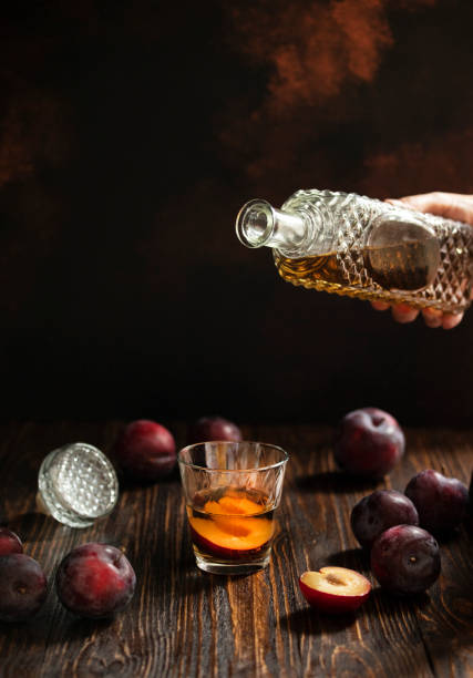 rakia o rakija tradizionale brandy di frutta balcanica. sljivovica di brandy di prugne in vetro e decanter su un tavolo di legno e sfondo scuro. rakia viene versata da una bottiglia in un bicchiere. verticale. spazio di copia - vodka hard liquor bottle palinka foto e immagini stock