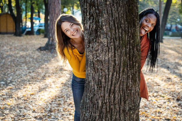 Multi ethnic friends in the autumn park behind tree