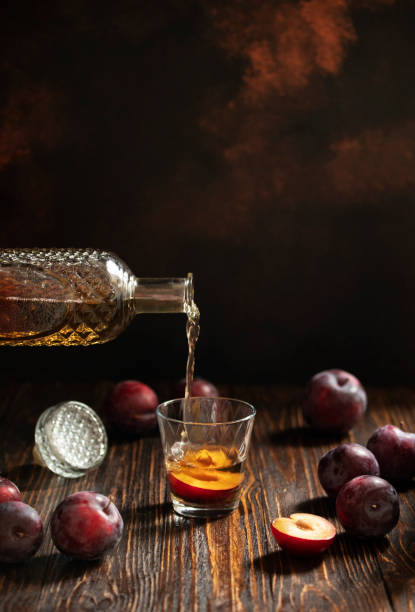 rakia o rakija tradizionale brandy di frutta balcanica. sljivovica di brandy di prugne in vetro e decanter su un tavolo di legno e sfondo scuro. rakia viene versata da una bottiglia in un bicchiere. verticale. spazio di copia - vodka hard liquor bottle palinka foto e immagini stock