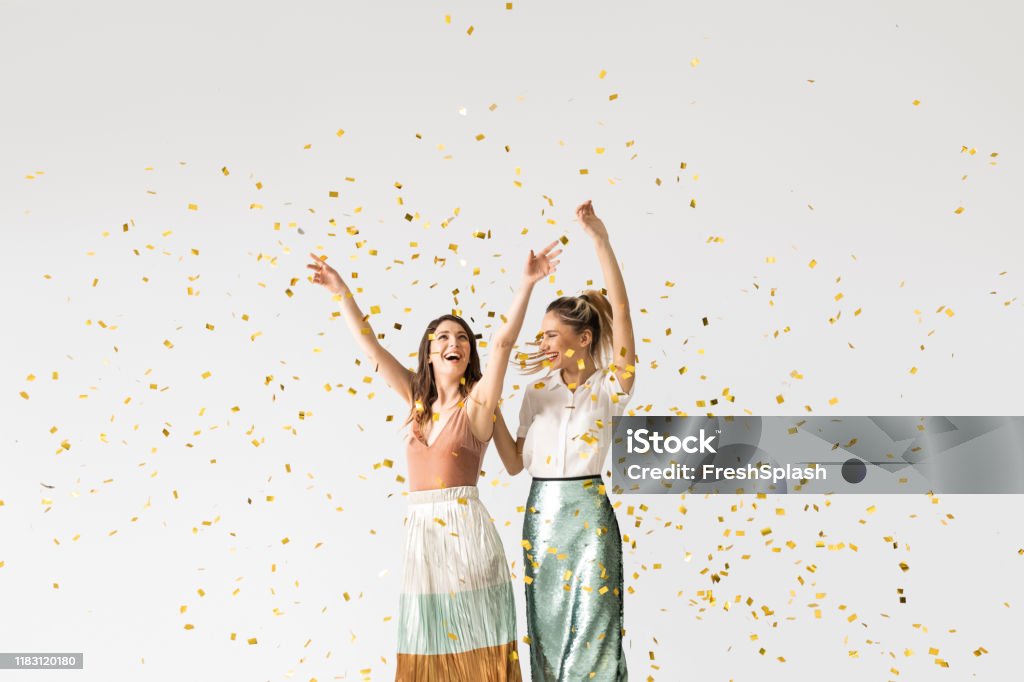 Party Girls Dancing Under Confetti Studio shot of two beautiful stylish young women smiling and dancing under confetti. Women Stock Photo