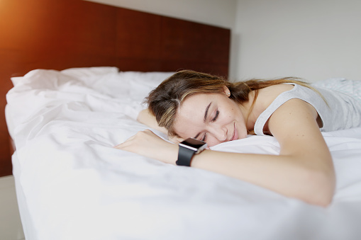 young woman sleeping uses Smartwatch with accurate sleep tracking stage breakdown laying at white bed. concept of new technologies for heart rate to track light or deep sleep