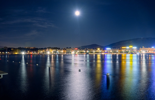 Full moon over Geneva at night. Panoramic view from the lake to the city center.