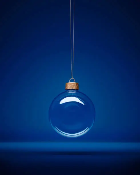 Glass christmas bauble hanging in front of luxury dark blue background. With copy Space for design or art greeting card.