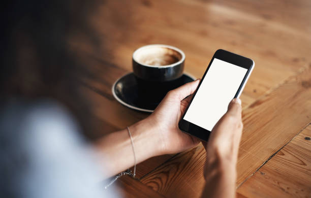 Cropped shot of an unrecognizable woman using her cellphone while having coffee at a cafe