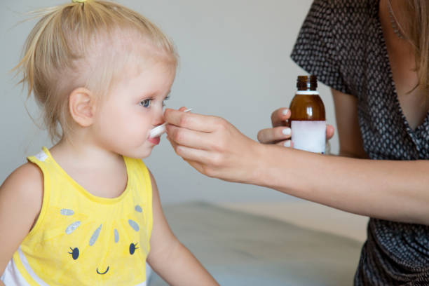 Mother giving daughter medicine on a spoon. Flu, fever or coughing symptoms. Mother giving a spoon of coughing syrup to her toddler girl. stock photo