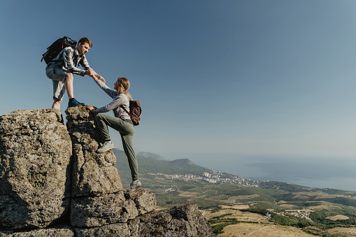 Young hiker an holding a woman hand helps to climb to the top of the mountain. The concept of help and support. Motivation for success