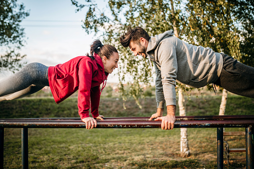 Young couple exercising in open air gym, doing push ups. Teamwork concept