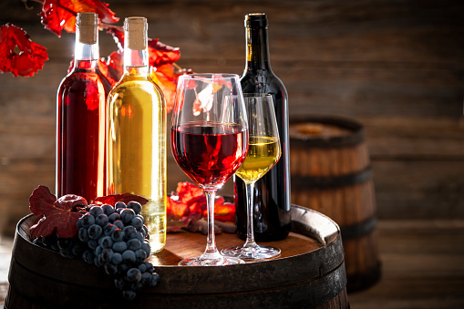 wine bottle and glass on wine oak barrel still on wooden background with red autumn grape leaves and cluster