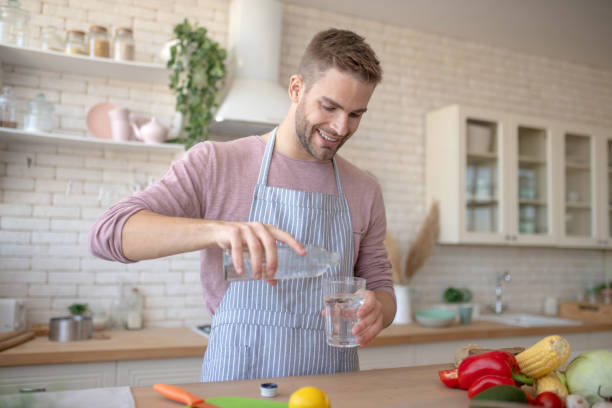 istock Man holding bottle of water while pouring it into glass 1183154089