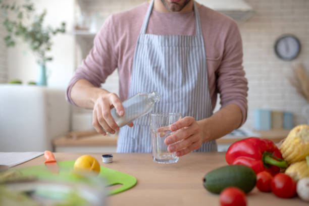 istock Man wearing apron pouring water into glass 1183154130