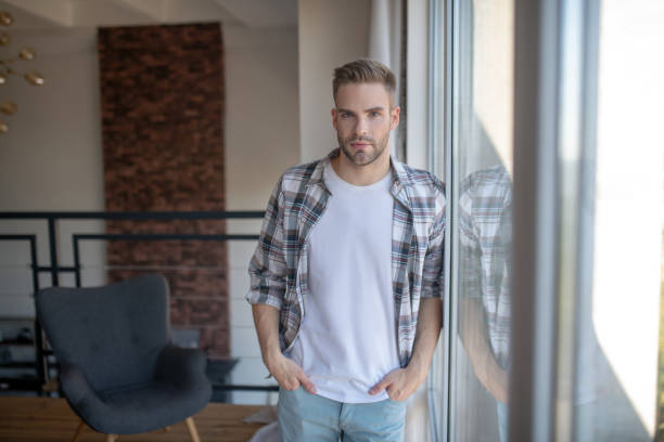 istock Stylish man wearing checked shirt standing near window 1183154190