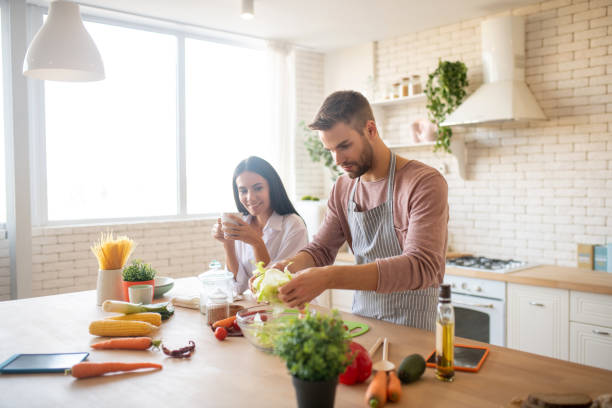 istock Wife drinking coffee and watching husband cooking salad 1183156310