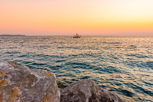 Sunset above the boat on Adriatic sea. Magic soft light and blue water near the Piran city, Slovenia. Stone rock in foreground.