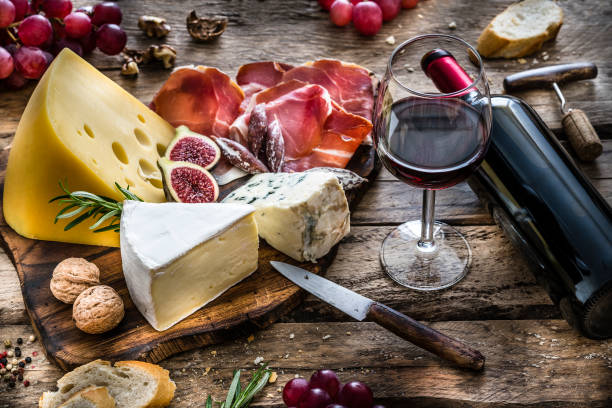 antipasto: vino rosso, formaggio e prosciutto stagionato su tavolo rustico in legno - cheese platter foto e immagini stock