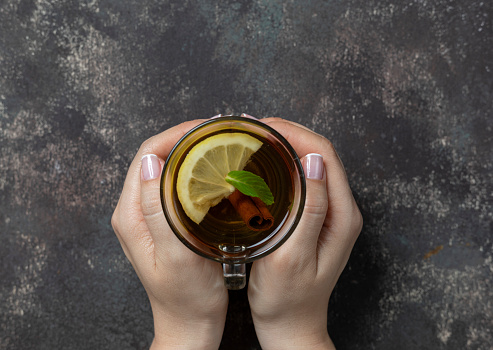 Herbal tea on dark background. Woman holding mug.