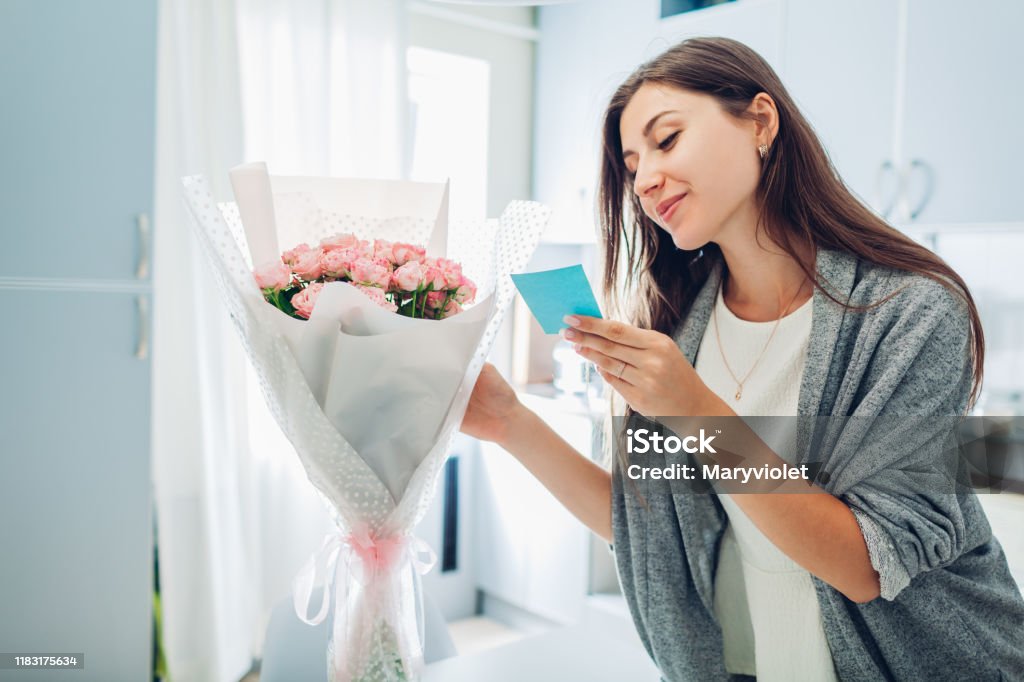 Woman found bouquet of flowers on kitchen and reading card on kitchen. Surprise. Present for holiday Woman found bouquet of flowers in vase on kitchen and reading card on kitchen. Surprise. Present for holiday Flower Stock Photo