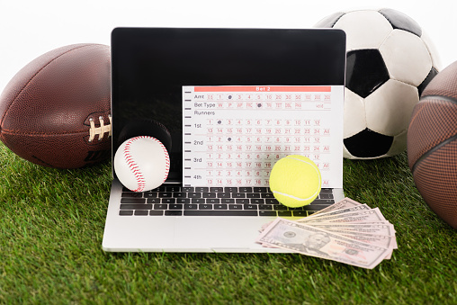 laptop near sports balls and betting list on green grass isolated on white, sports betting concept