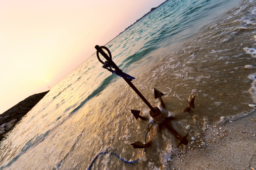 a damaged anchor by the beach with motion sea water, image taken in dubai during sunset.