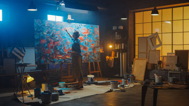 재능있는 여성 작가는 추상적 인 유화에 노력하고, 페인트 브러시의 넓은 스트로크와 함께 그녀는 현대 걸작을 만듭니다. 이젤 조명에 큰 캔버스 스탠드 어둡고 지저분한 크리에이티브 스튜디� - painted image expressionism people abstract 뉴스 사진 이미지