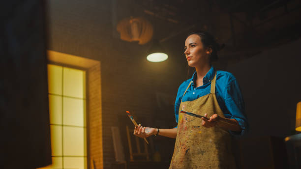 istock Talented Female Artist Drawing with Paint Brush Energetically, She Creates Modern Masterpiece of the Oil Painting. Creative Studio with Large Canvas of Striking Colors. Low Angle Portrait 1183183656
