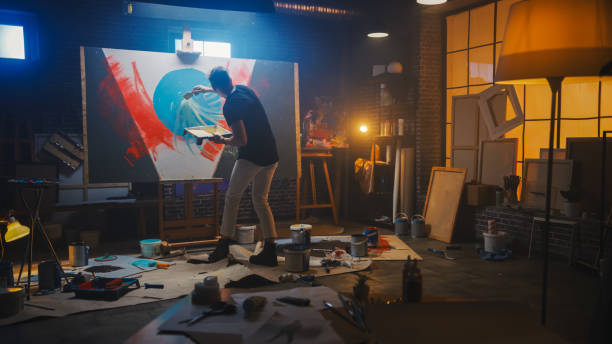 Talented Artist Working on Abstract Painting, Uses Tray Palette to Mix Colors and Paint Brush To Create Daringly Emotional Modern Picture. Dark Creative Studio, Large Canvas Stands on Easel Illuminated artista talentoso que trabaja en la pintura abstracta, utiliza la paleta de bandejas para mezclar colores y pincel de pintura para crear una imagen moderna atrevidamente emocional. dark creative studio, grandes soportes de lona en easel iluminado