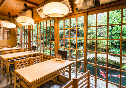 This is a photograph of the interior of a restaurant with wooden tables and chairs and a garden view in Kyoto, Japan.